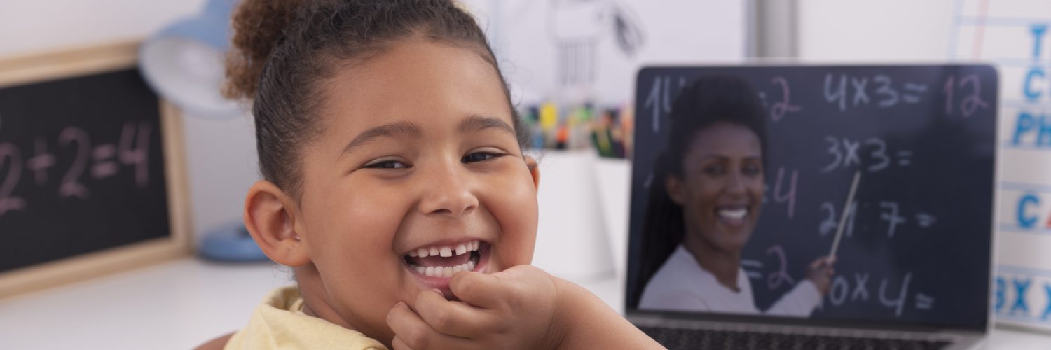 Child smiling while using her laptop.