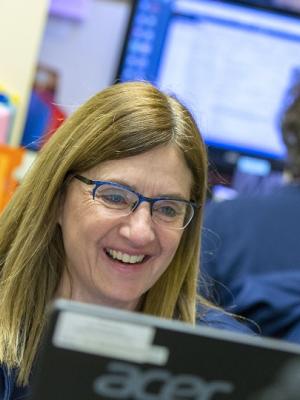 Medical office associate Laura Bjanes smiles as she types on a laptop. She is wearing glasses and a sweat jacket. Her hair is straight and past her shoulders.