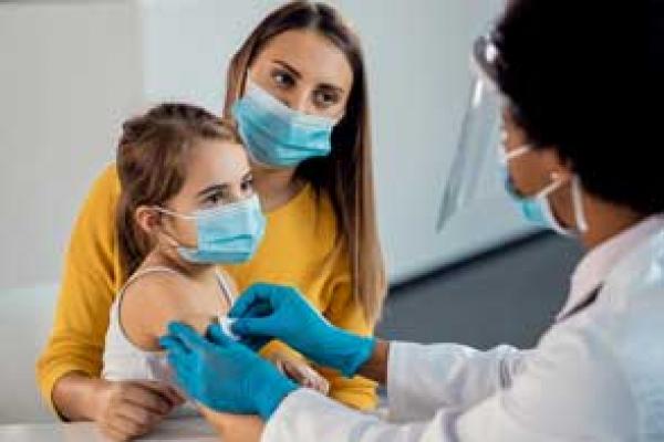 Female doctor placing adhesive bandage on little girl's arm after vaccination. Focus is on girl.