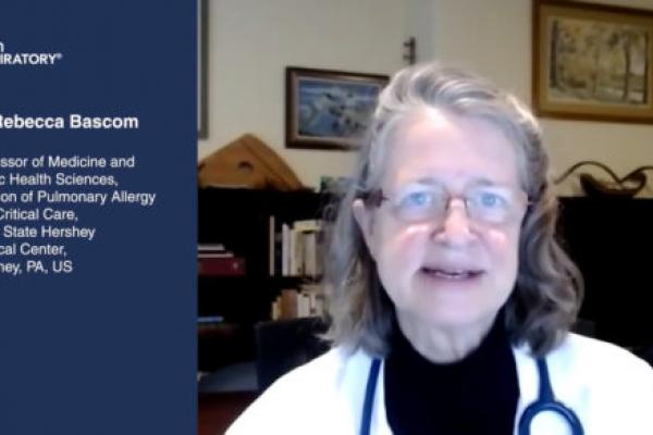 Dr. Rebecca Bascom, wearing a white coat and glasses, speaks in a room lined with bookcases and picture frames.