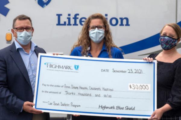 Three people smile while holding a big check