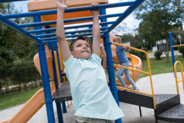 A young girl hangs from playground equipment.