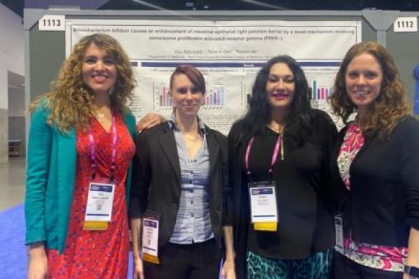 Dr. Raz Abdulqadir, left, gastroenterology fellow; Jessica Engers, research technologist; Dr. Rana Al-Sadi, researcher and assistant professor of medicine; and Dr. Lauren Kaminsky, allergy and immunology fellow, stand for a group photo in front of a research poster filled with text and graphics that was presented at the global Digestive Disease Week conference.