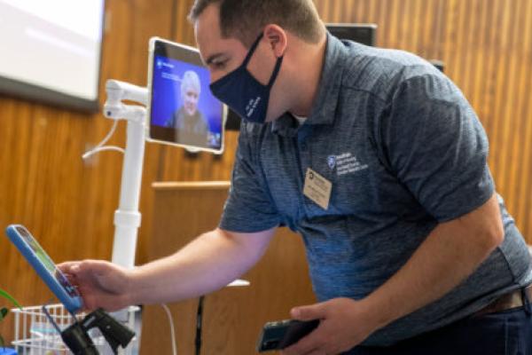 A man leans over a smart phone, demonstrating how it is used to connect patients to experts via telehealth