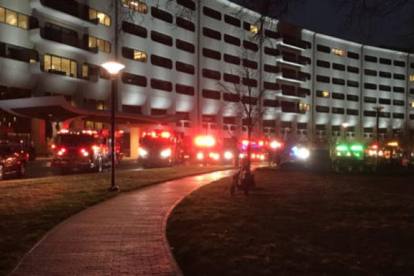 Several emergency vehicles and tow trucks with flashing lights park along the crescent at Hershey Medical Center, at dusk.