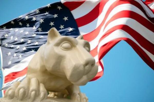 A Nittany Lion statue in the foreground, with an American flag in the background.