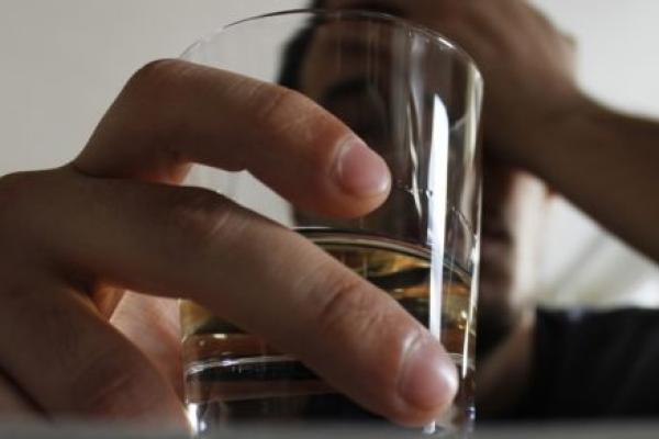 A man cradles his head with one and holds a glass of liquor with the other.