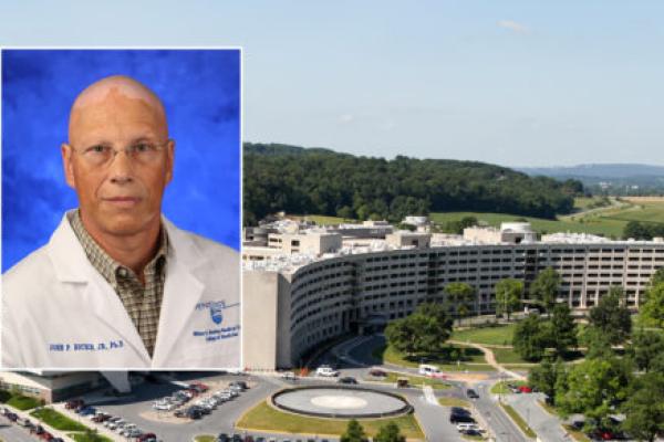 A head and shoulders professional portrait of John Richie against a background photo of Penn State College of Medicine