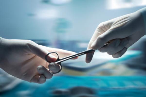 Close-up of two gloved hands handing off a piece of equipment in an operating room.