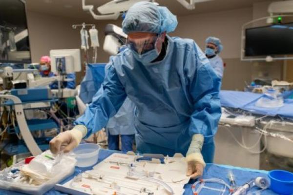 A man in surgical scrubs leans over equipment in an operating room.