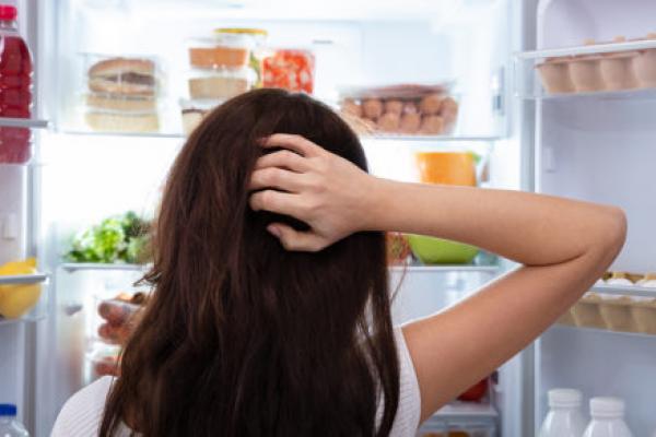 困惑的女人在打开的冰箱里寻找食物