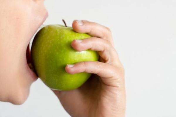 A close-up of a child biting into a green apple.