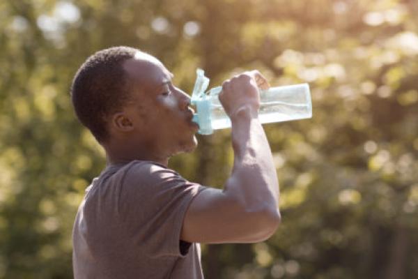 An overheated man drinks water from a bottle in a park.