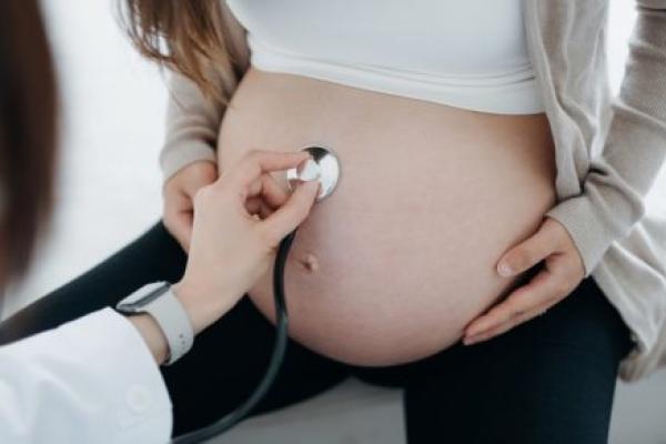 Close up of a health care provider doing checkup on a pregnant woman, examining the belly with stethoscope.