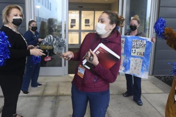 Someone dressed as the Nittany lion and others in masks raise pompoms and cheer another woman n a mask.