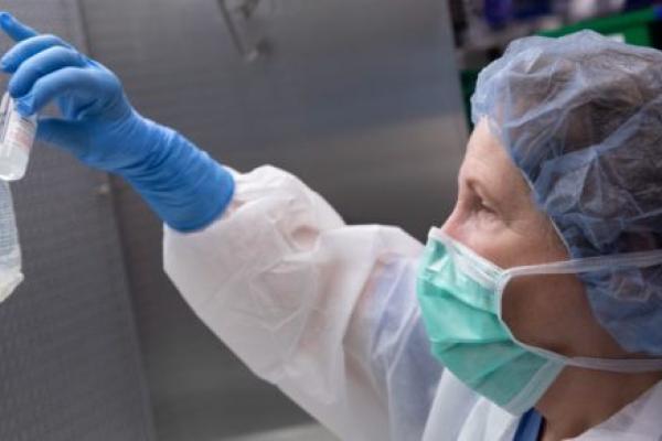 A masked, female pharmacy technician wearing various items of personal protective equipment prepares remdesivir for a patient in the pharmacy.