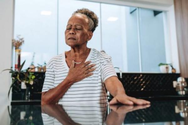 An elderly woman puts her hand over in chest and grimaces in pain.