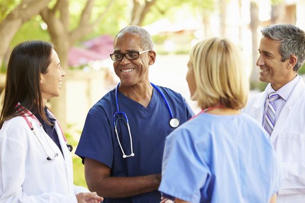 Three Doctors Standing Outside A Hospital Chatting To Each Other Laughing